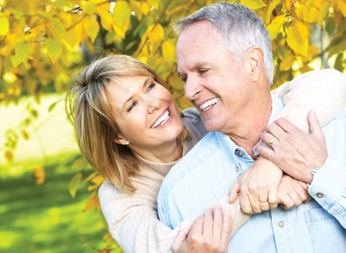 A woman and man embrace against a yellow and green fall foliage background