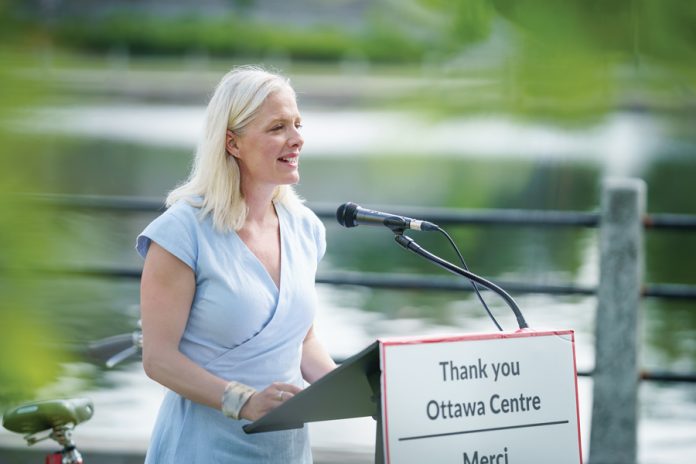 Catherine McKenna stands at a podium in Ottawa next to the Rideau Canal on a summer day