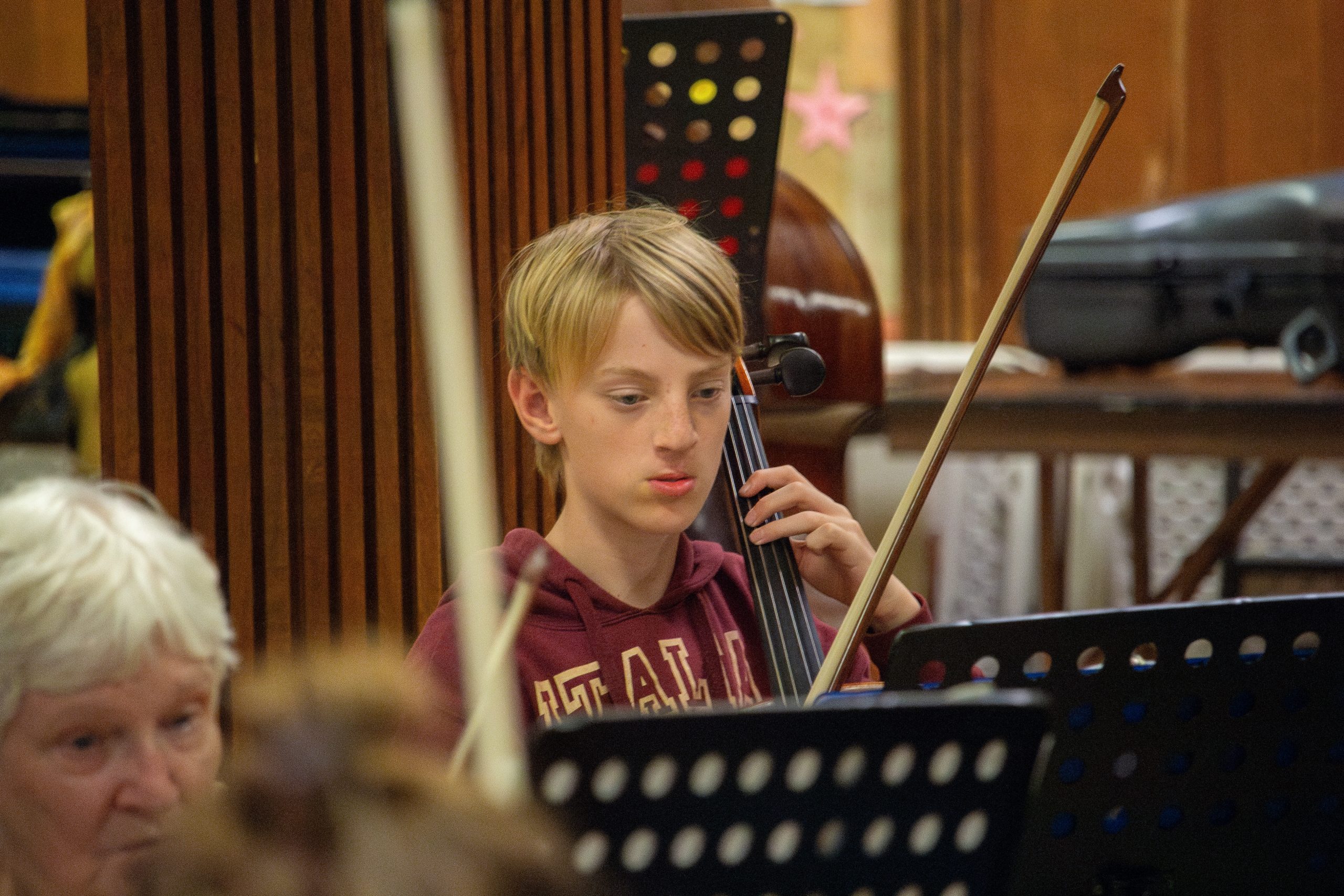 Edwin is pictured playing his cello. He’s wearing a burgundy sweater. 