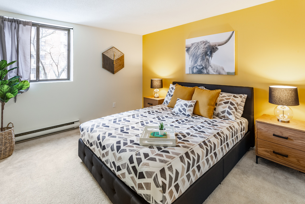 A bedroom is pictured with a yellow wall behind a large bed. An artwork with a bull hangs behind it.