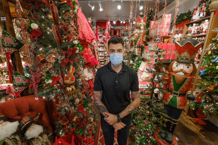 Audy Czigler stands in the middle of a decorated Tinseltown store in Hintonburg.|Many Irish-themed ornaments hang on the wall|A blue ornament hangs on a white tree at Tinseltown|White and green lit tree decorations at Tinseltown|A Santa decoration wearing green.|Three caroler decorations at Tinseltown|An ornament of a dog wearing a Santa hat