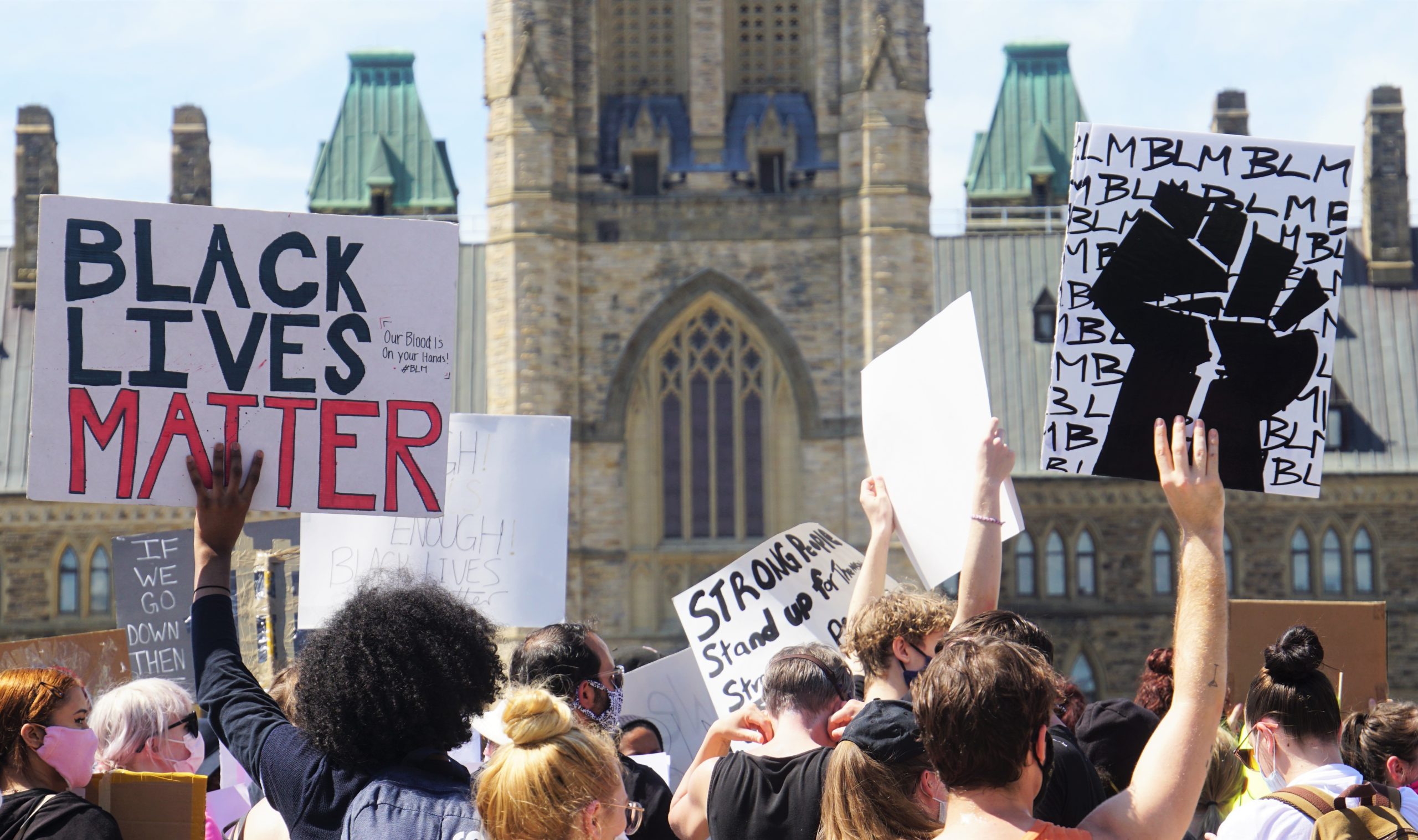 Hundreds are seen holding signs outside of the parliament buildings on a summer sunny day