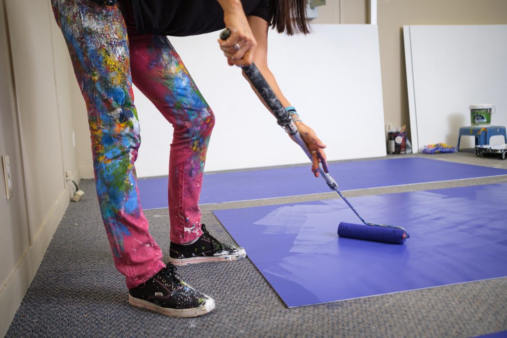 A close up of Claudia Salguero painting a blue panel on the floor