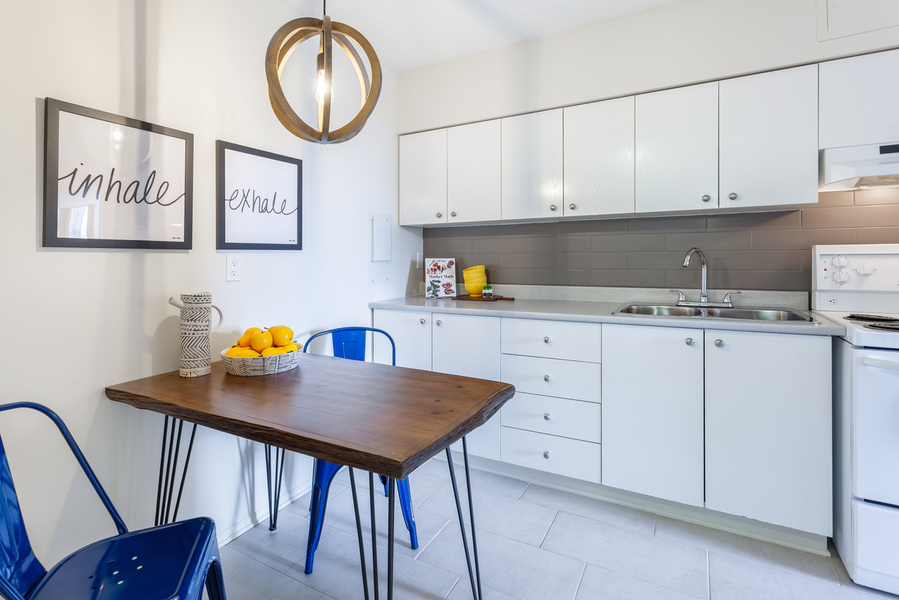 A white kitchen is seen with a wooden table and two cobalt-coloured chairs