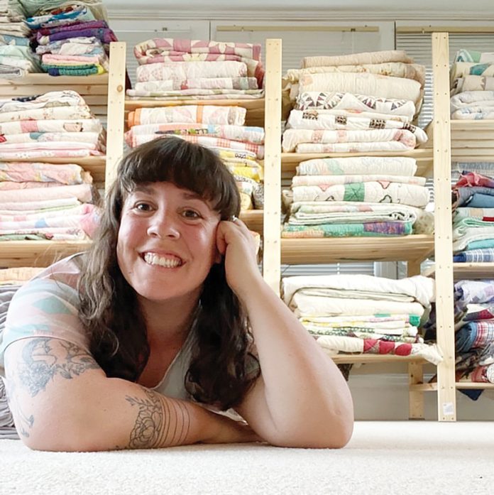 Stephanie Hylarides sits at a table in front of a wall of folded clothing