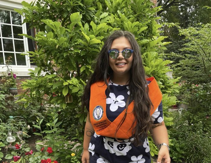 A woman stands in front of a garden at a house with green