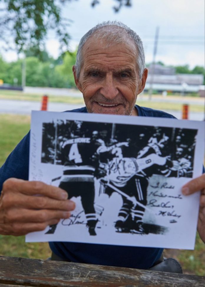 A photo of Rod Zaine holding up a picture of himself playing hockey against Gordie Howe and his sons Mark and Marty.