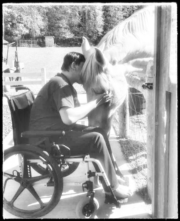 An individual in a wheel chair pets a horse in a black and white photo