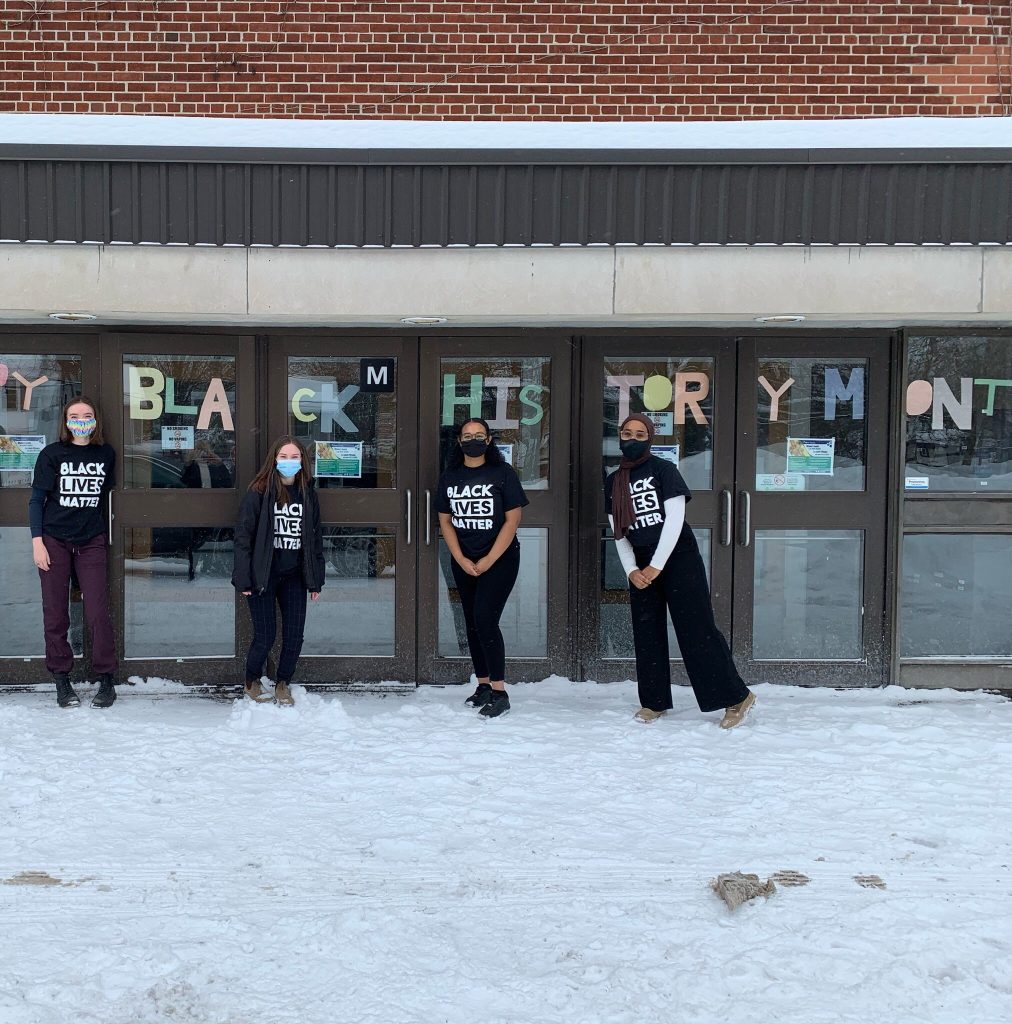 Four students stand outside of Nepean High School on a snow covered field wearing Black Lives Matter t-shirts for Black History Month