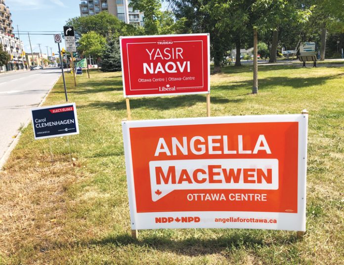 Four election signs are seen on a lawn in a park in Westboro on a sunny day|