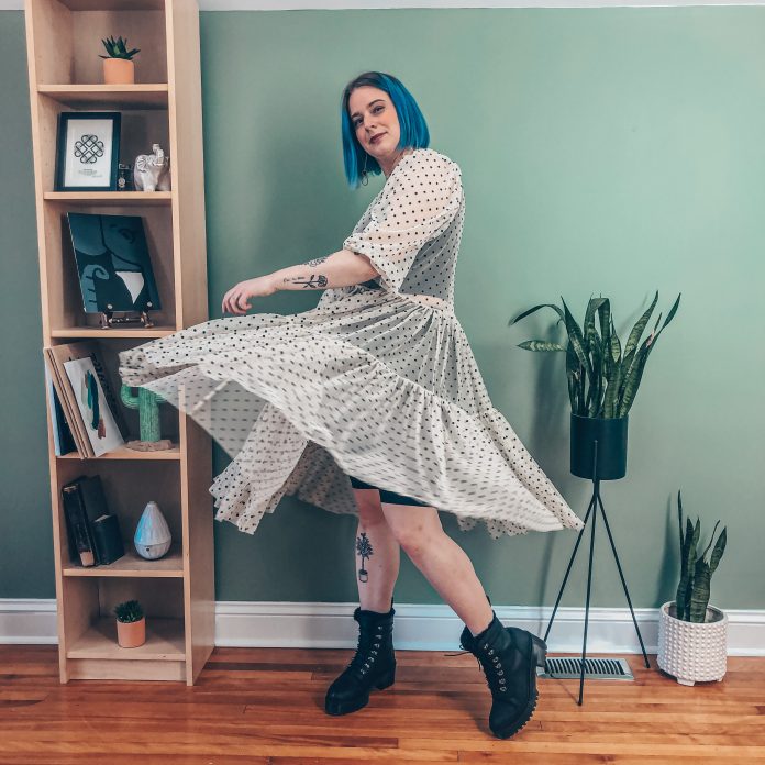 Rebecca Clark Kipfer twirls in a white dress while standing next to a wooden bookshelf and two plants against a green wall