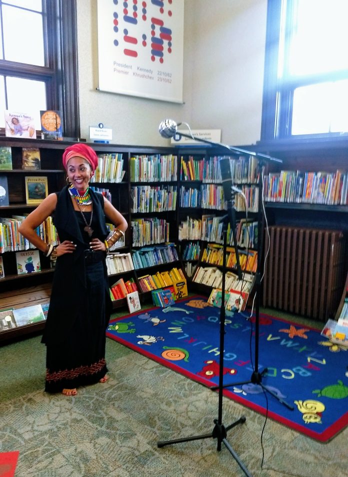 A woman stands in front of a microphone in a library|