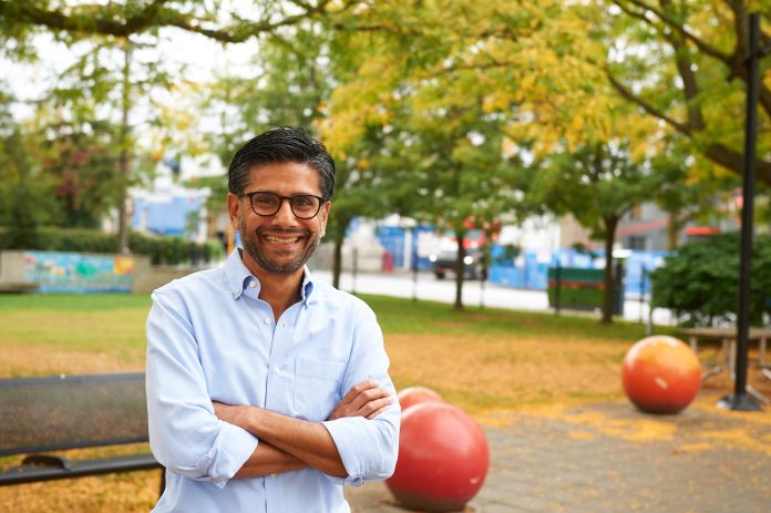 A man stands with a public park behind him in Ottawa Centre. There are colourful fall leaves all around.|