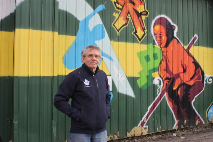 A man stands in front of a wall of graffiti on Scott Street outside the curling club|The exterior of the Granite Curling Club on a sunny spring day in Ottawa