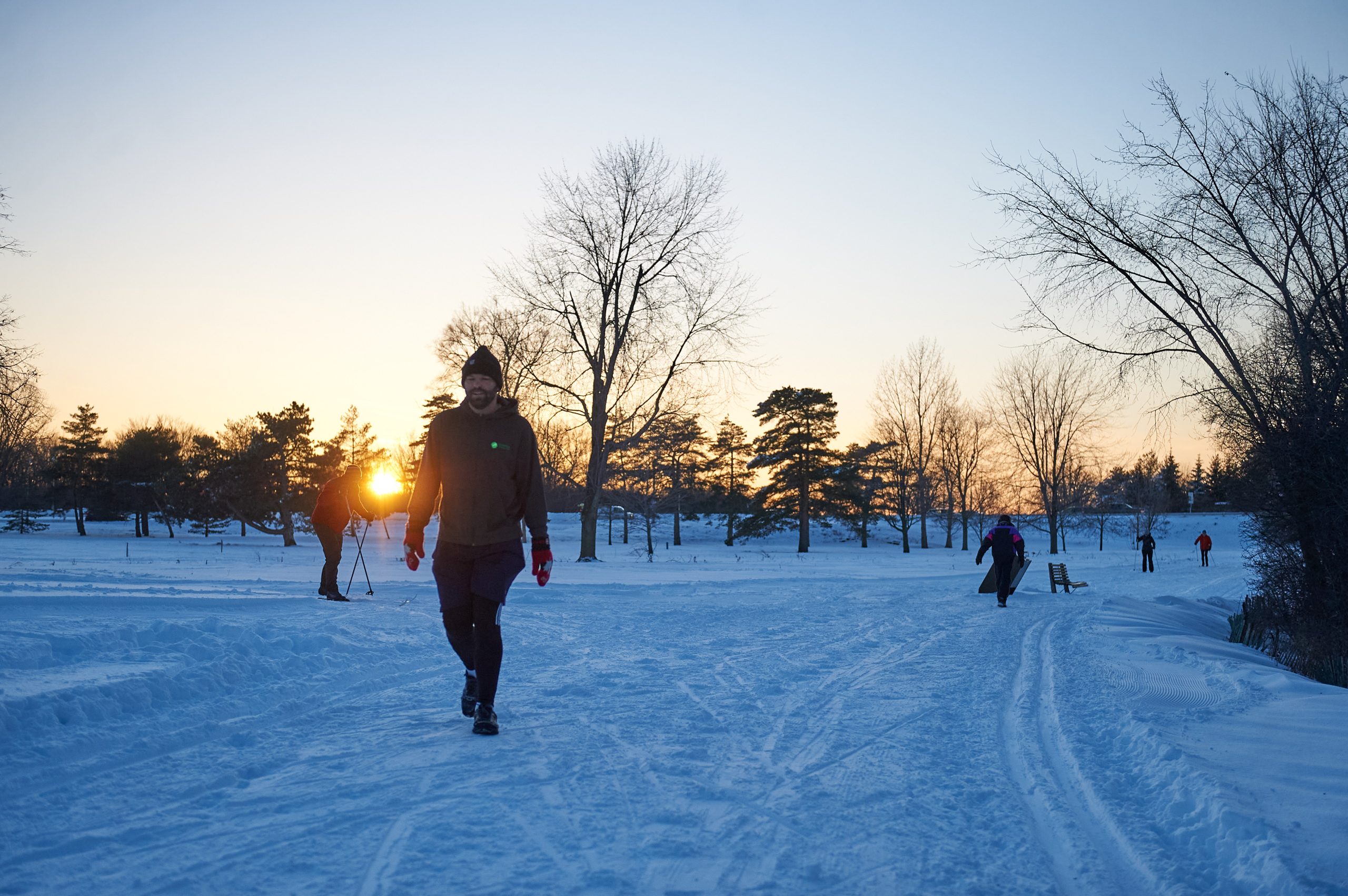 People walk and ski along Kichi Sibi Winter Trail in winter at sunset