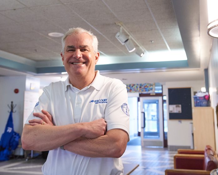 A man wearing a white shirt stands with his arms crossed at Dovercourt Recreation Centre.||