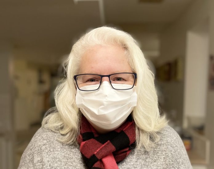 A professional headshot of a woman with white hair wearing a white face mask