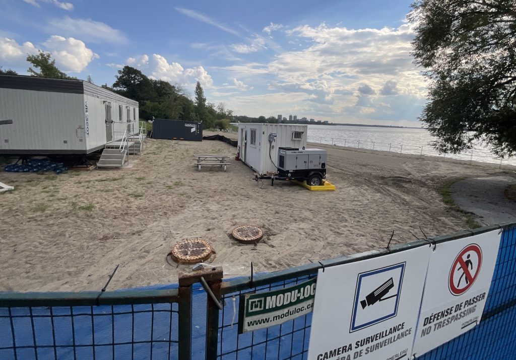 White construction trailers on Westboro beach on a sunny day. There is a blue fence in the background.