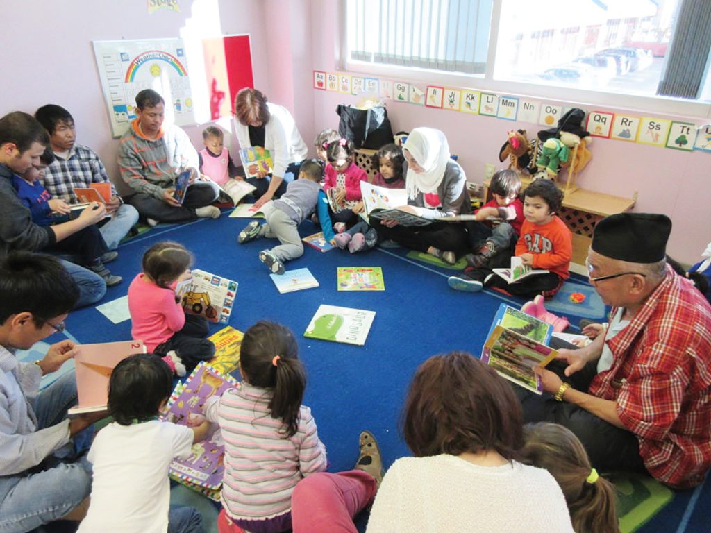 A group of adults and children participate in Ottawa Community Immigrant Services Organization's school program while sitting on the floor with textbooks and writing utensils