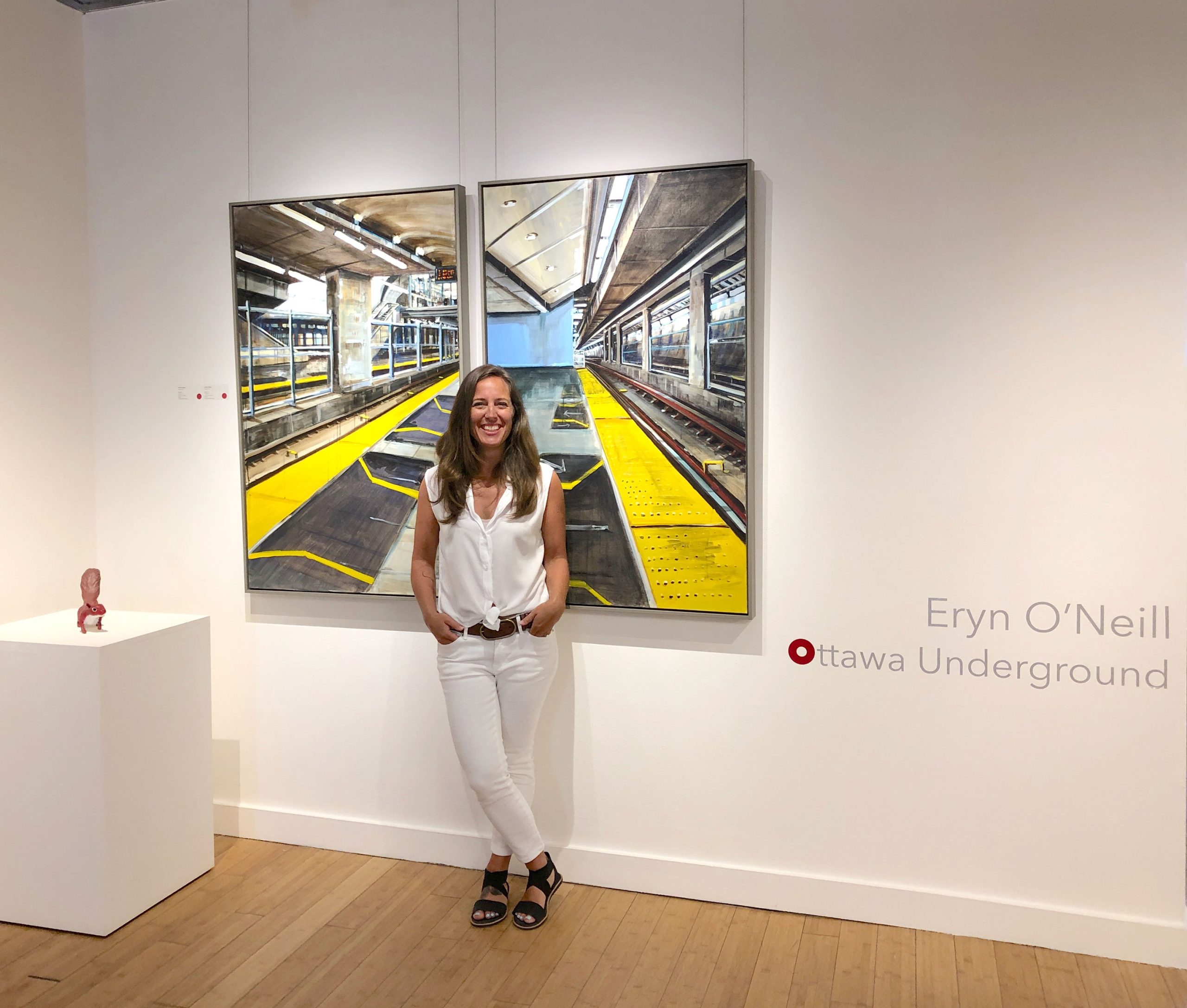 A photo of local Artist Eryn O’Neill standing in front of her newest body of work, Ottawa Underground, on display in Hintonburg.