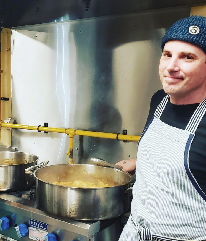 Simon Bell is seen next to a big pot of soup in the kitchen at the Parkdale Food Centre|A volunteer holds a soup bowl and plate with bread on it at the Parkdale Food Centre