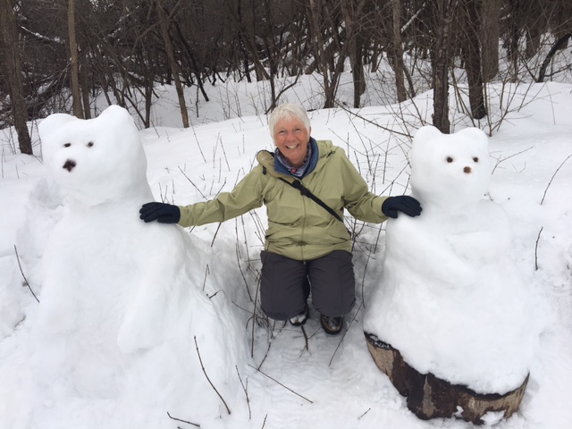 A woman wearing a green snow jacket and grey snow pants sits between two bears made of snow in Ottawa