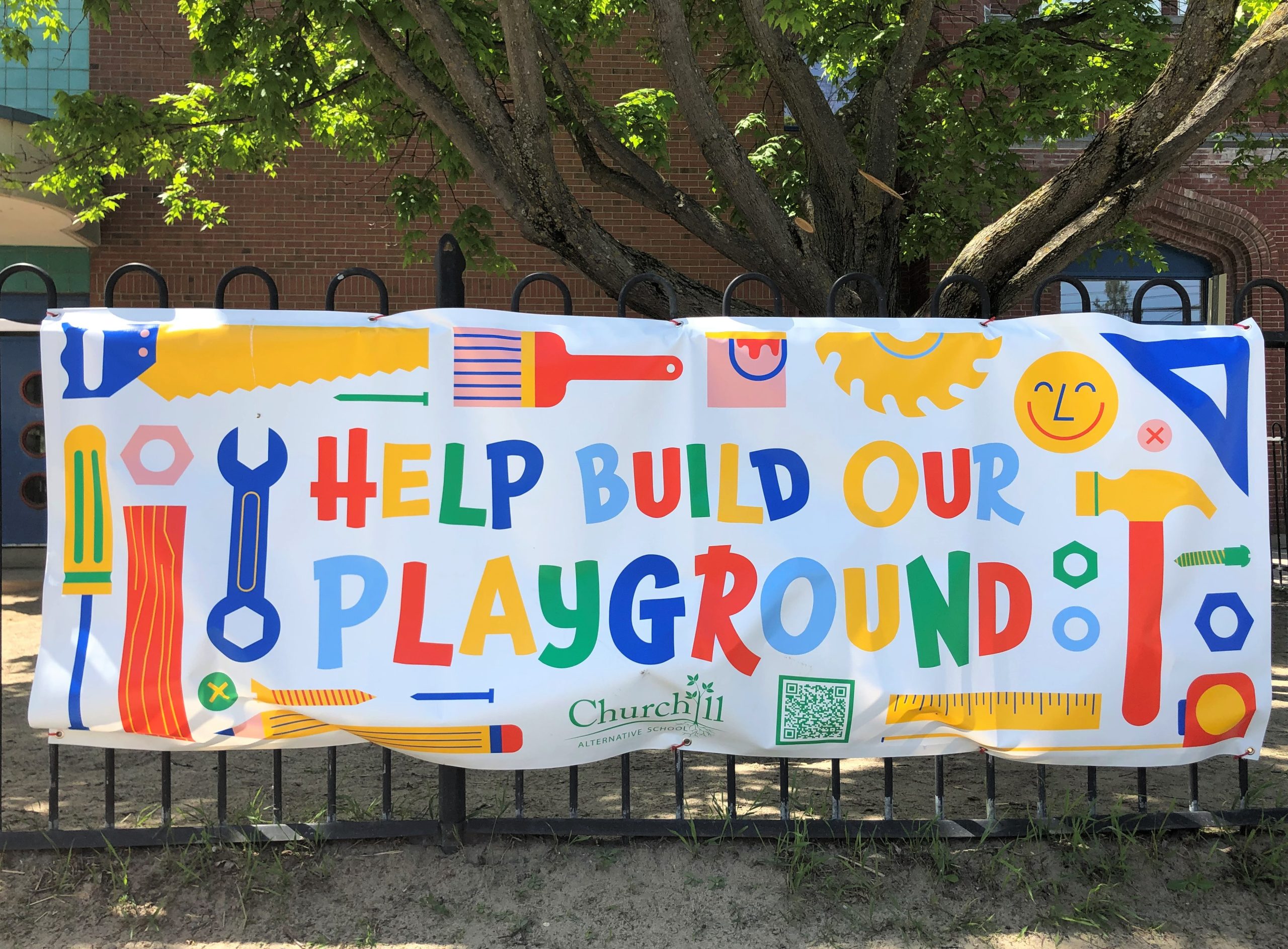 A multicoloured banner outside Churchill Alternative School reads "Help build our playground."