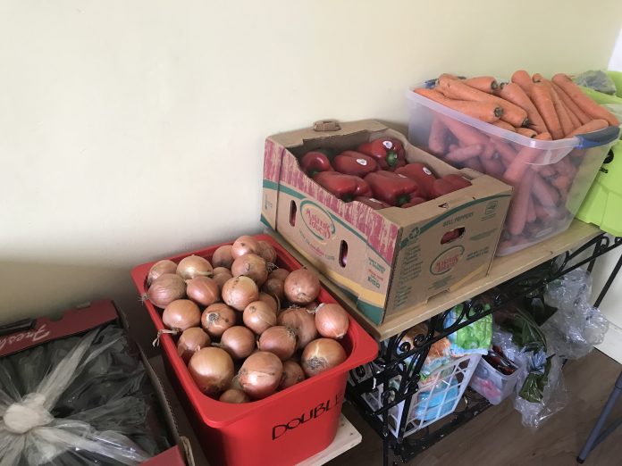 A row of bins on a table that hold fruit and vegetables.|