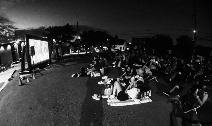 A black and white photo showing hundreds of people watching an outdoor movie.|A black and white photo of two women wearing Capital Pop-Up Cinema shirts.