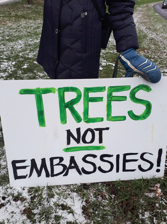 A white protest sign is held up by a gloved hand. The sign reads 