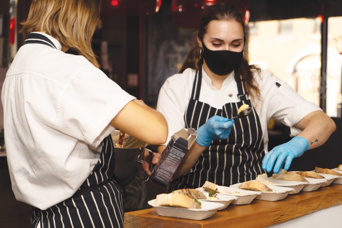 Two chefs prepare dishes at a Carefor event. Both are wearing black masks and blue gloves.|||