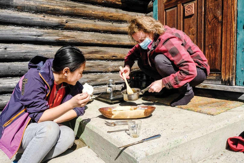 Two women make maple syrup on a doorstep of a wooden log house in Westboro