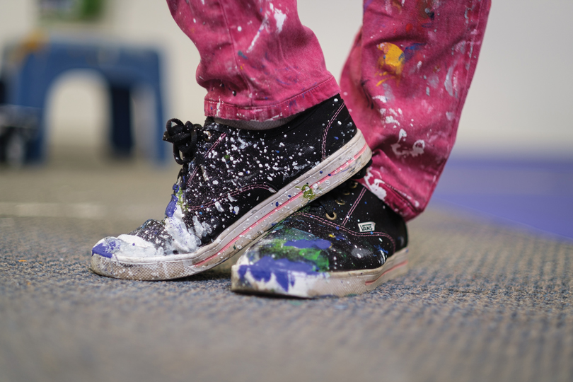 A close up of black sneakers and pink pants that are splattered with paint.