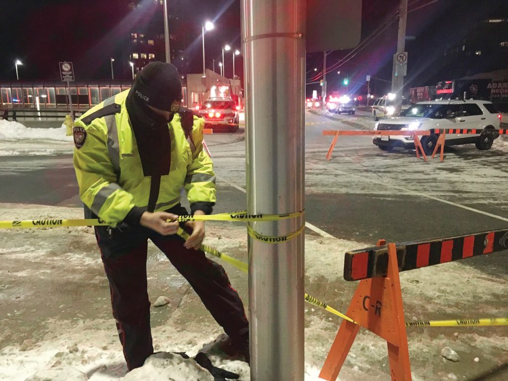 A police officer stands near a pole at the Westboro bus station and tapes off an accident scene