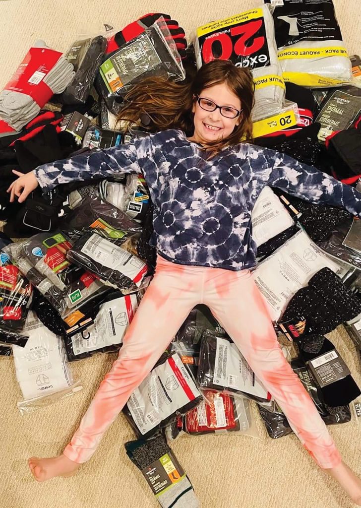 An 8-year-old girl lays on top of a pile of items to be donated like socks and mittens