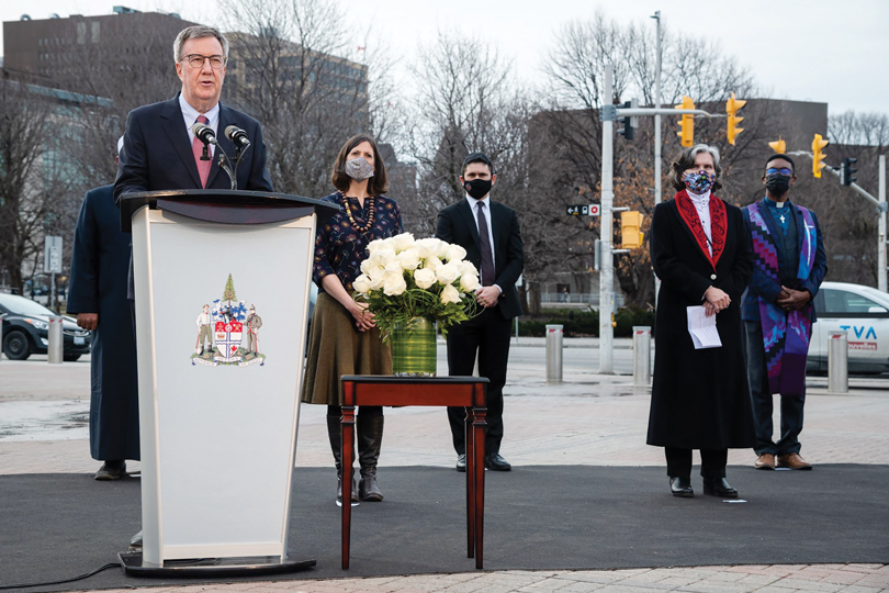 Mayor Jim Watson stands at a podium outside city hall on an overcast day in Ottawa with religious leaders standing behind him standing six feet apart and wearing masks