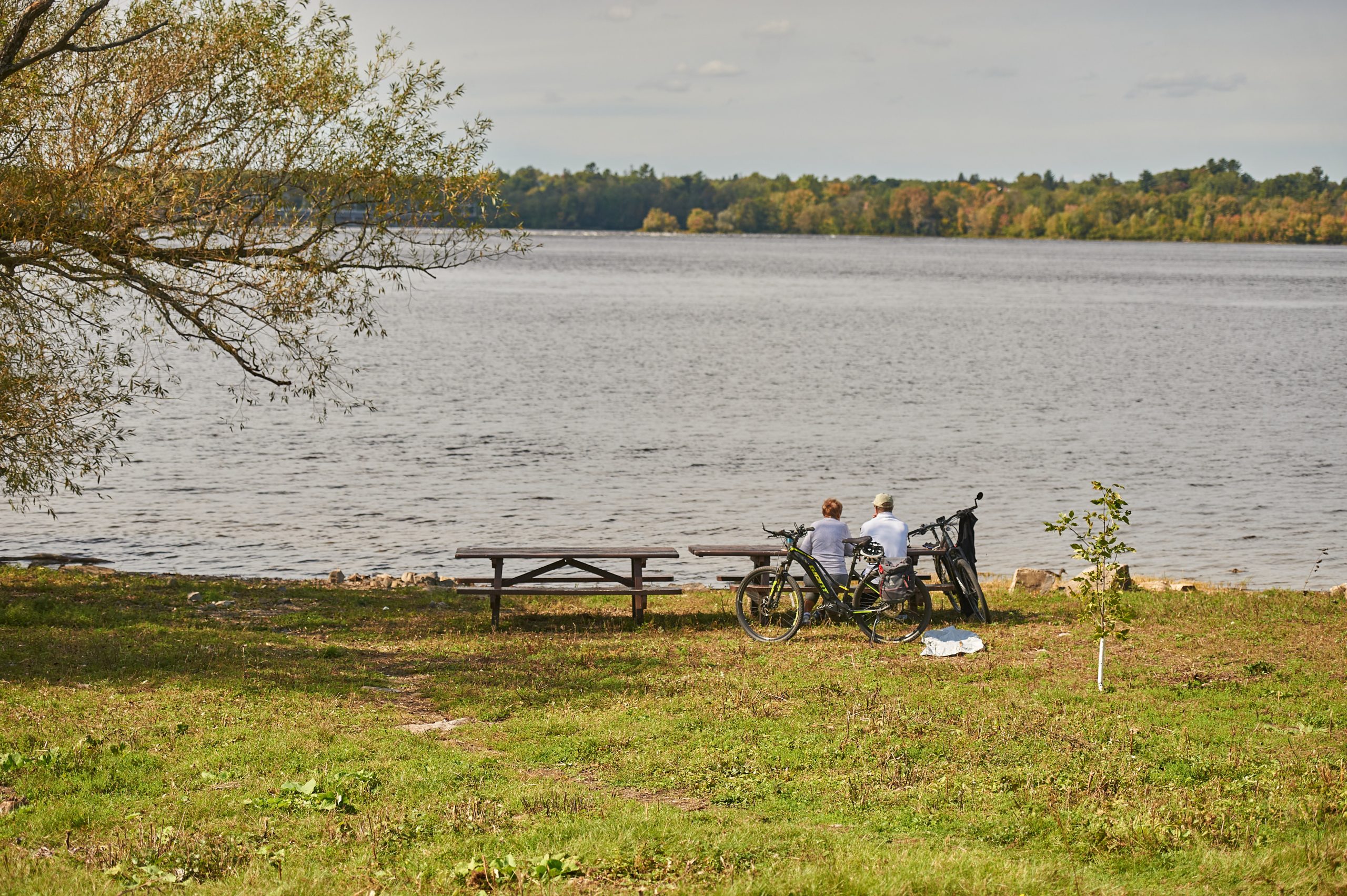 Two people sit at a bench and take a break from their bike ride along the Ottawa River