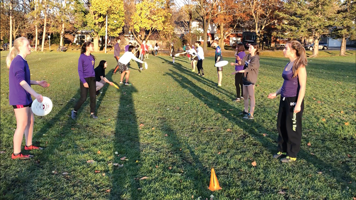 A group of youth frisbee players throw frisbees back and forth in a line at McKellar Park