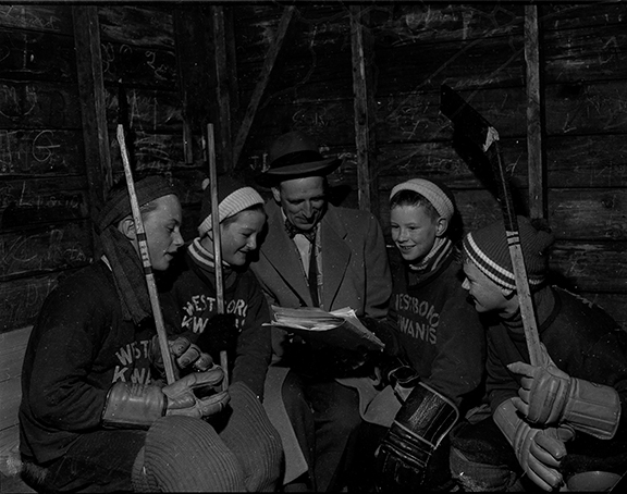 A group of young hockey players gather around an adult coach in 1956 Ottawa in a black and white photo