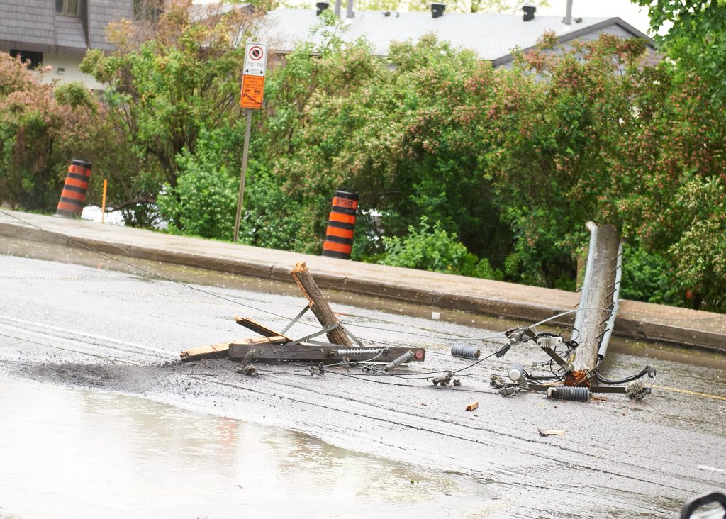 Wires and metal are seen on the ground following a storm. There are bushes in the background and rain puddles in the foreground.