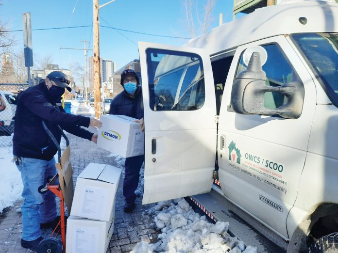 Two volunteers load a van with food boxes on a snowy day in Ottawa.|A volunteer fills boxes with food at Ottawa West Community Support's office.