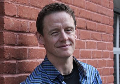 A headshot of Joel Harden against a red brick building.