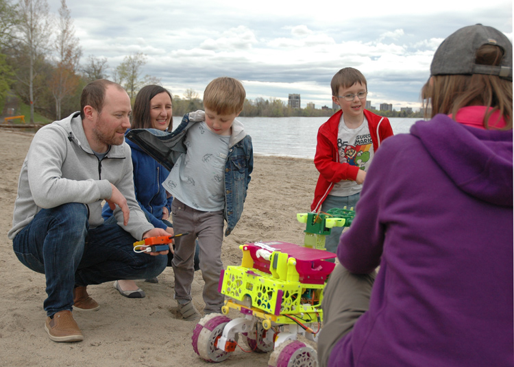 Owen Columbus, Magdalena Columbus and their sons Theo and Miles gather around the bots as Erin explains how they work.