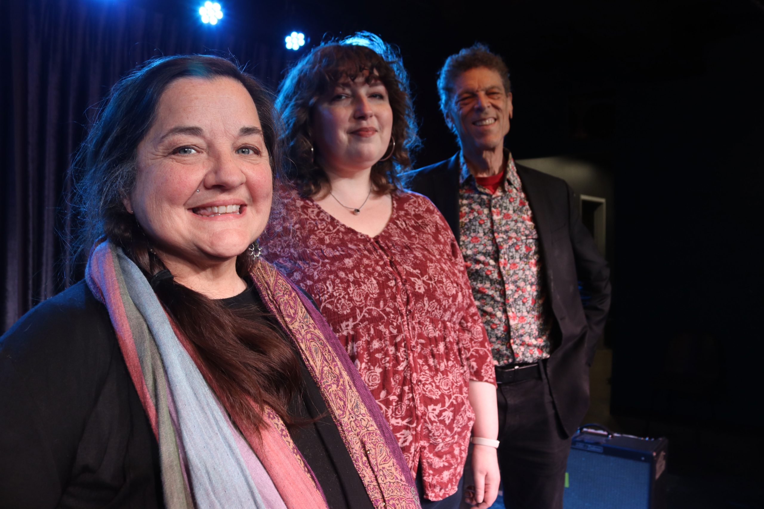 Three people pose for a photograph on a state with a curtain begins. Nicole is in the front.