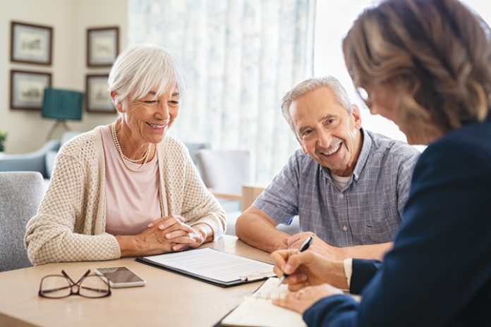 An elderly couple sits at a table with a real estate agent.