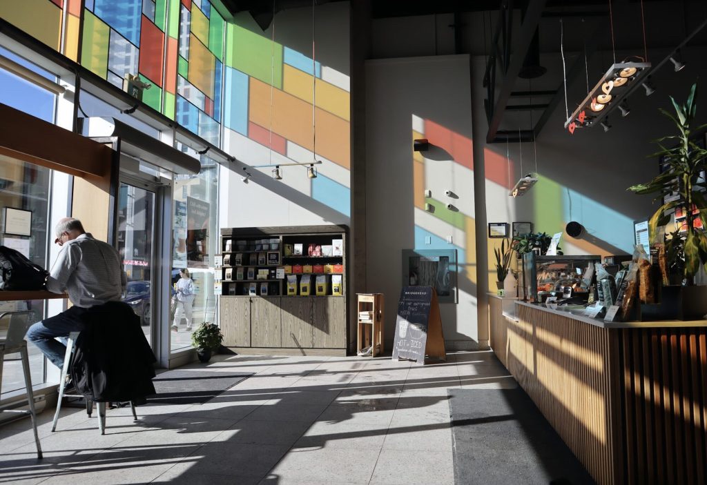 A very sun lit coffee shop with reflections of colourful stained glass windows reflecting on the walls. 