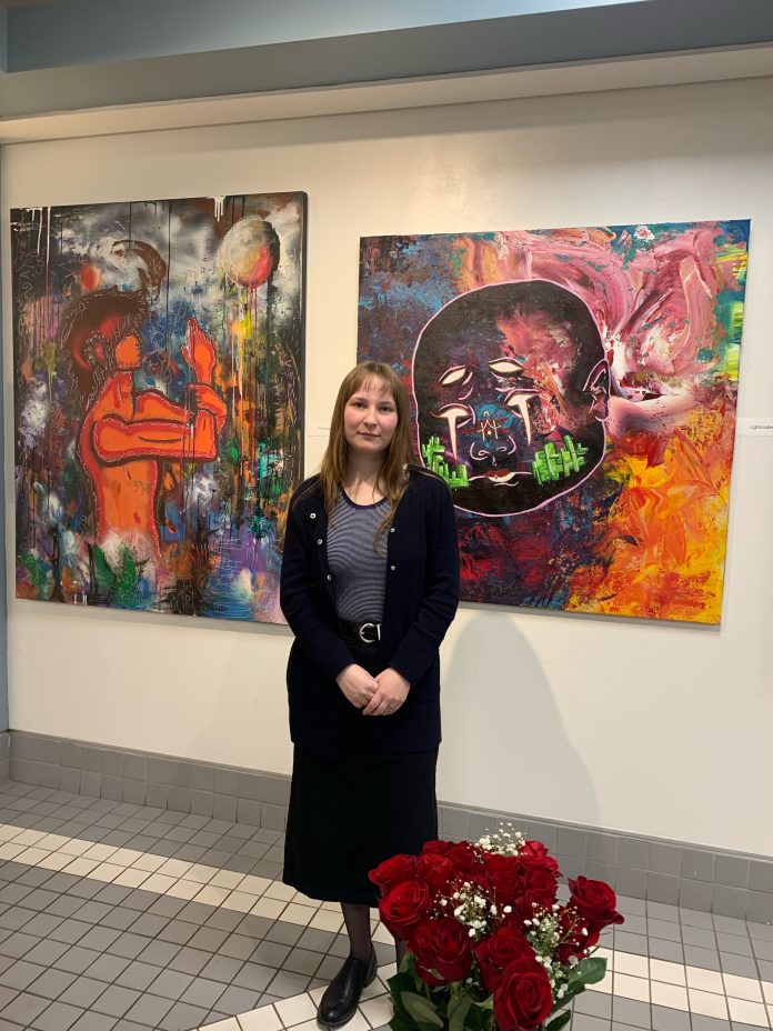 A fuel stands in front of colourful paintings that hang on the wall. Red Roses can be seen in the bottom right of the photo