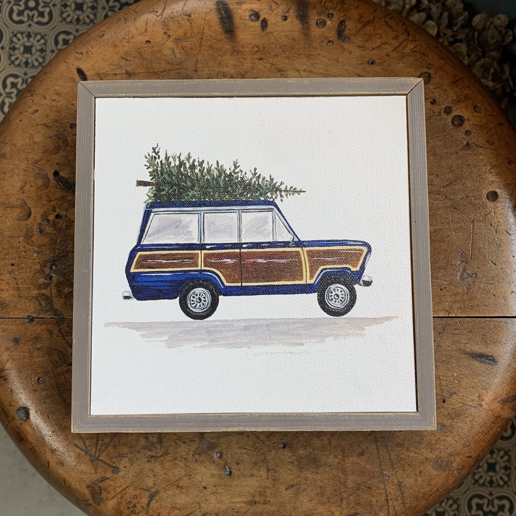 A framed picture of a station wagon carrying a Christmas tree on its roof.