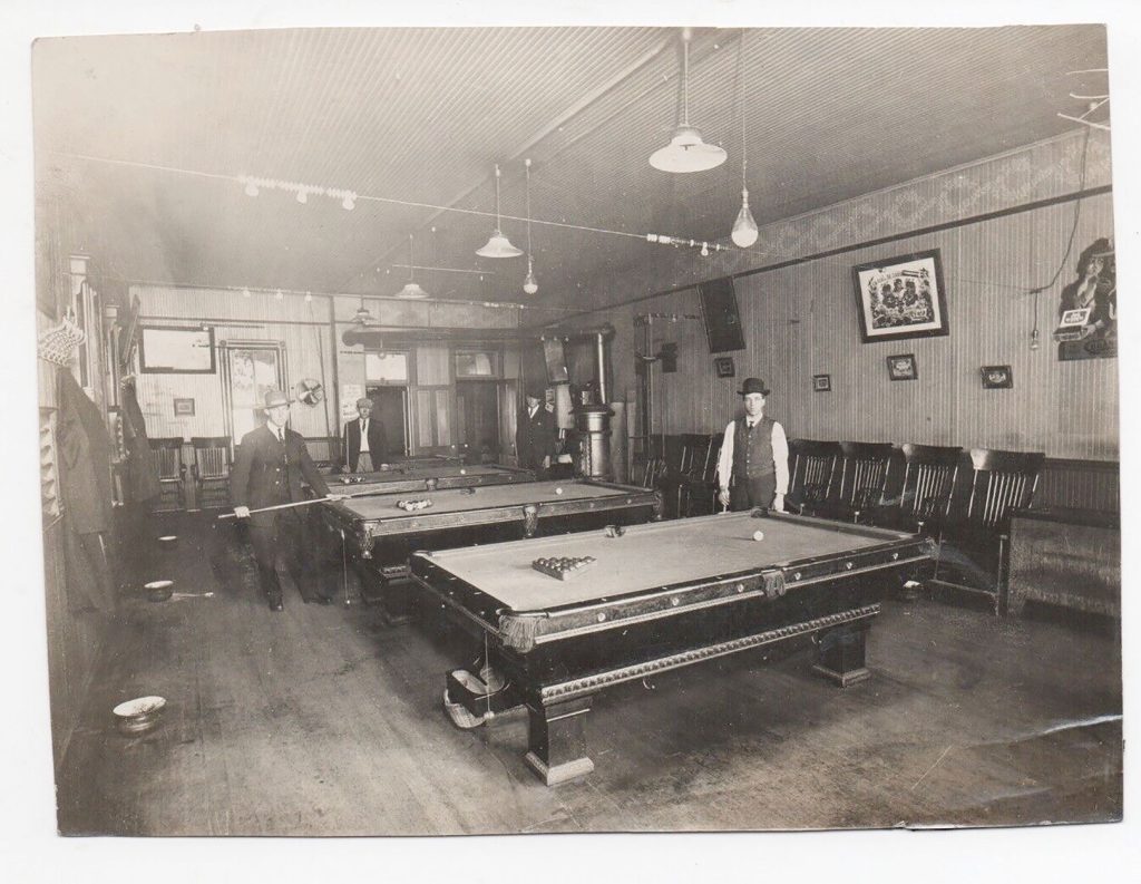 An old black and white photo showing three gentleman playing pool. 