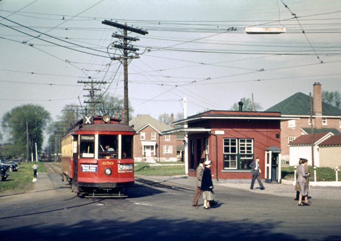 Ah old coloured photograph showing a red streetcar. People are crossing the street.